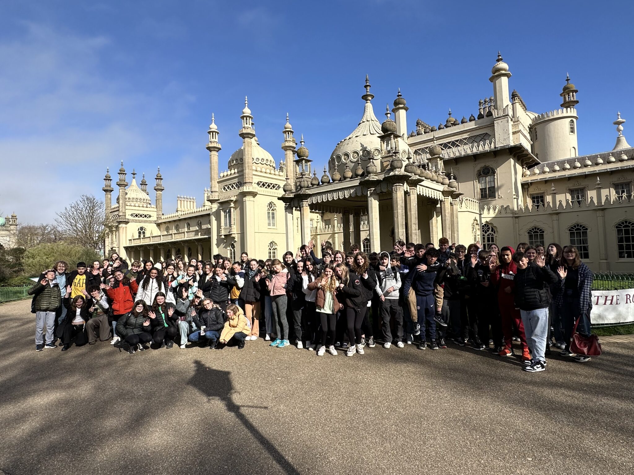 A large group of people stands in front of the ornate Royal Pavilion under a clear blue sky.