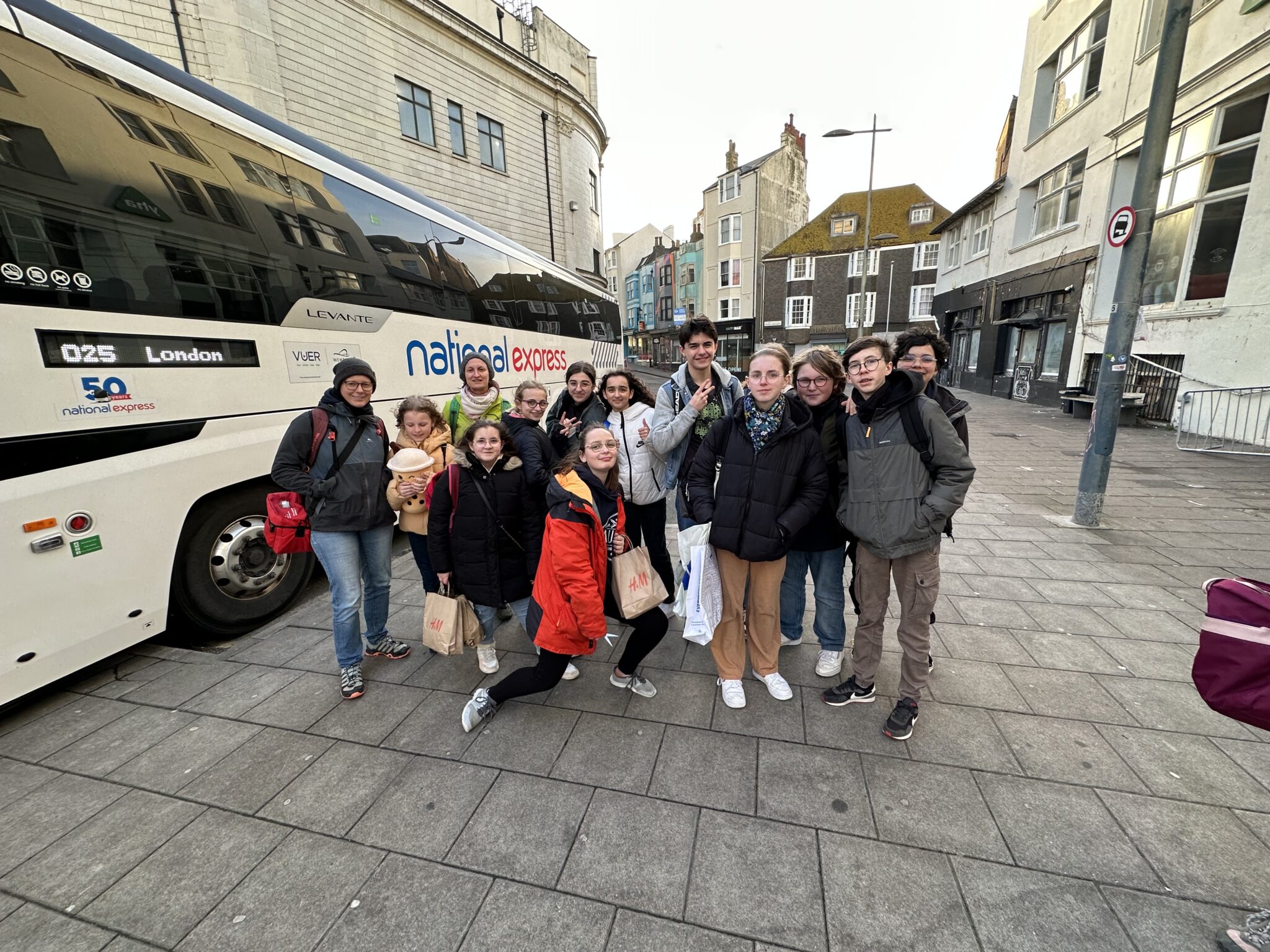 Group of people standing near a National Express bus on a city street, posing for a photo in winter clothing.
