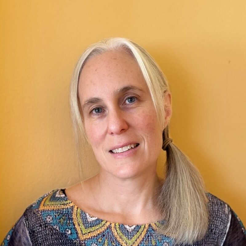 Person in colorful mandala-patterned shirt, yellow background.